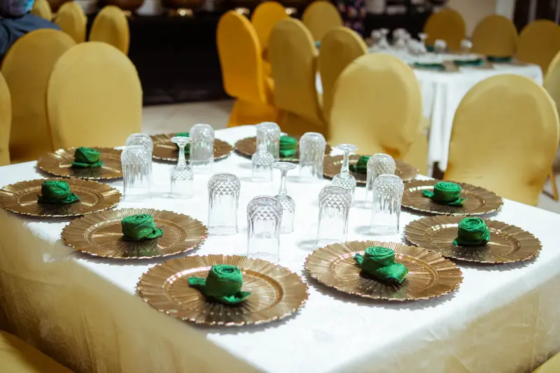 Gold sunburst charger plates with emerald rose napkins and crystal glassware on a banquet table