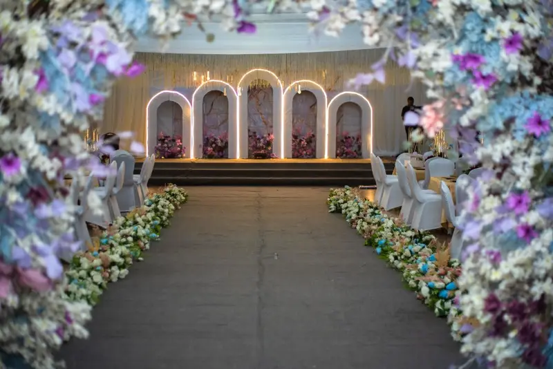 Floral archway framing an illuminated arched stage along a flower-lined aisle