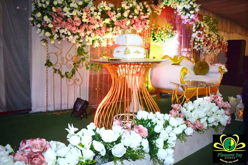 Two-tier white and gold wedding cake on a gold pedestal with floral backdrop